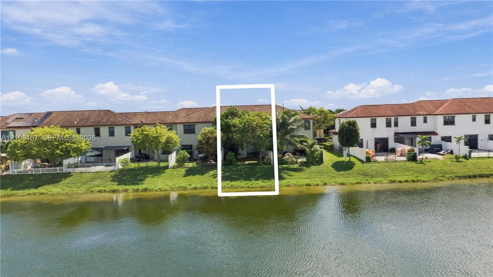Waterfront exterior featuring a multi-story stucco facade, tiled roof, and expansive lawn bordering the canal