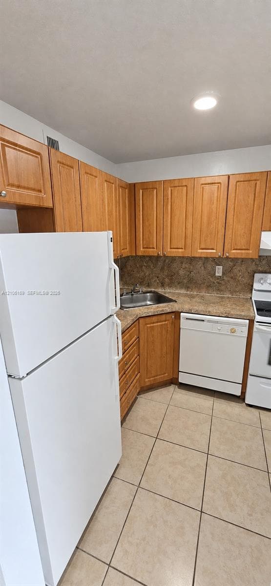 Kitchen featuring light-tone wood cabinetry, stone-finish countertops, tile flooring, and white appliances