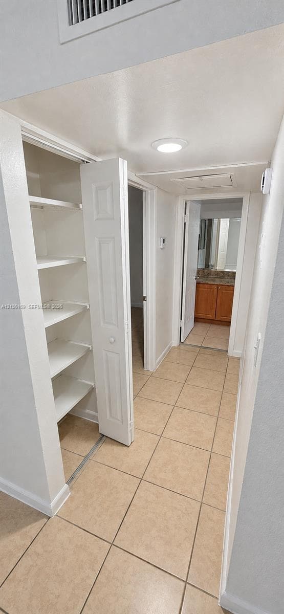 Hallway featuring tile flooring, built-in storage shelving with folding doors, and recessed lighting