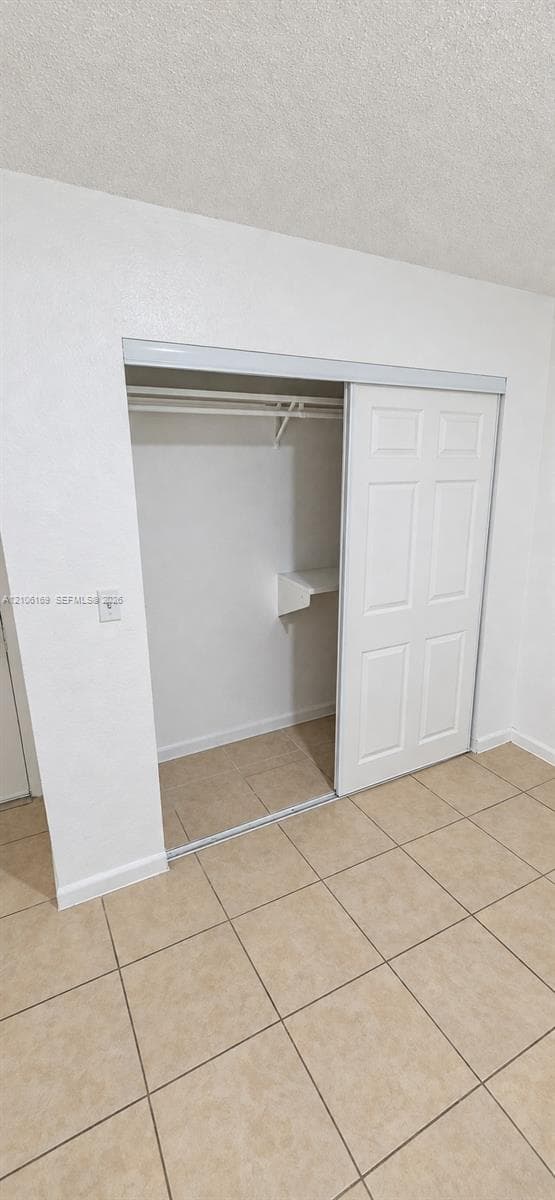 Closet featuring dual sliding six-panel doors, integrated shelving, and a hanging rod, finished with neutral tile flooring