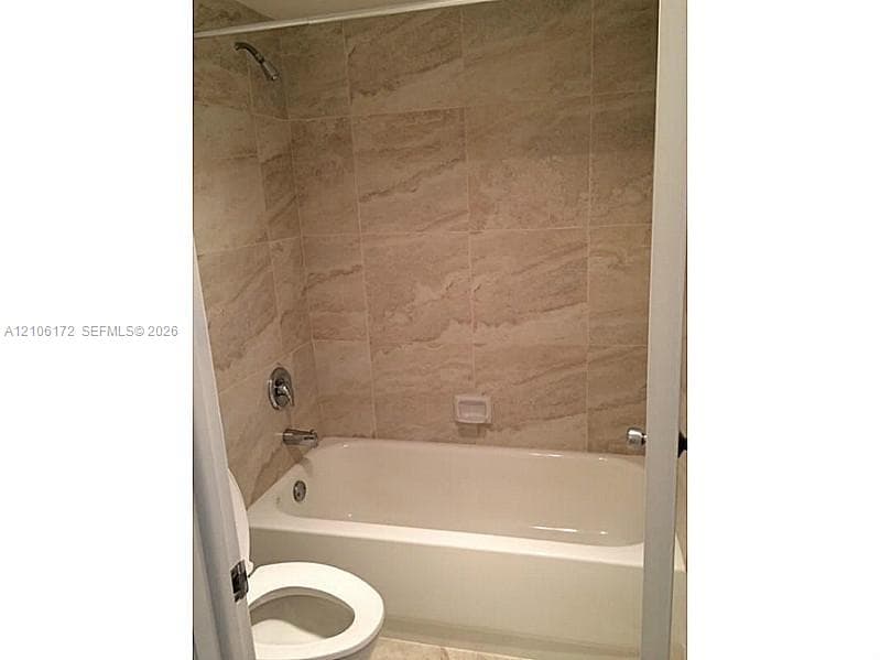 Full-height shower surround with neutral-toned oversized tile, white bathtub, chrome shower fixture, and recessed soap dish