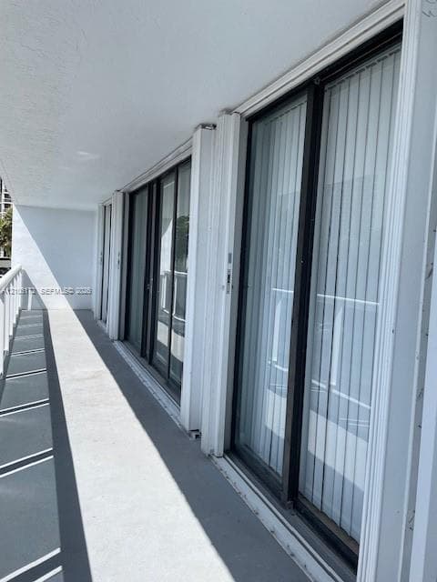 Covered balcony featuring concrete flooring, white metal railing, and multiple floor-to-ceiling sliding glass doors with dark frames