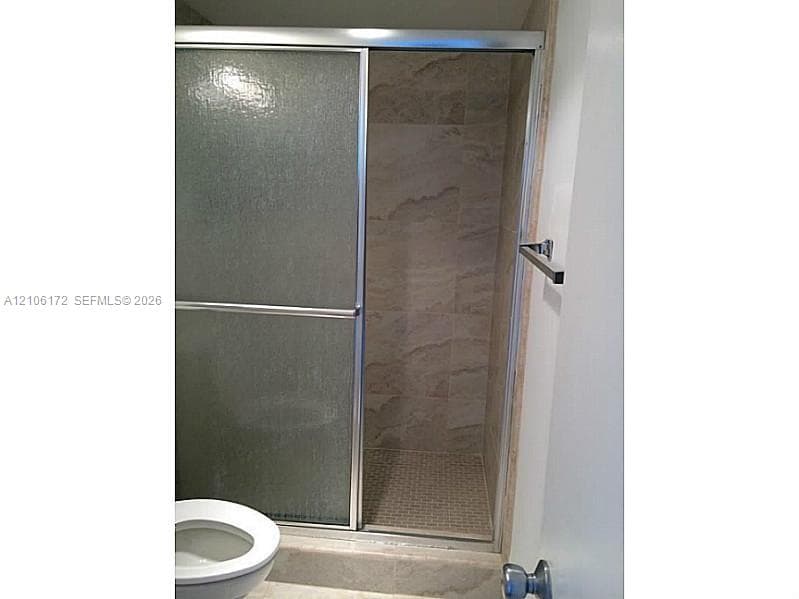 Walk-in shower featuring a sliding glass door, full-height stone-finish wall tile, mosaic tile shower floor, and metallic hardware