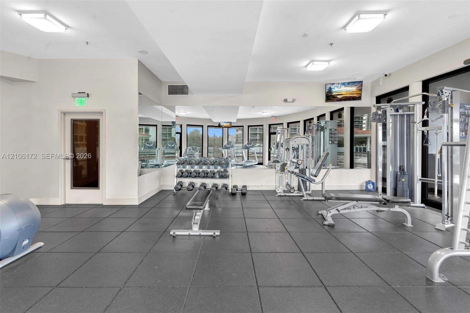 Fitness center featuring rubberized tile flooring, floor-to-ceiling mirrors, recessed lighting, and multiple windows