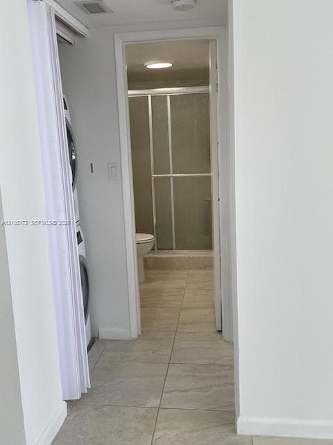 Stacked laundry unit housed in a bi-fold door closet, tile flooring, and a walk-in shower with a framed glass enclosure