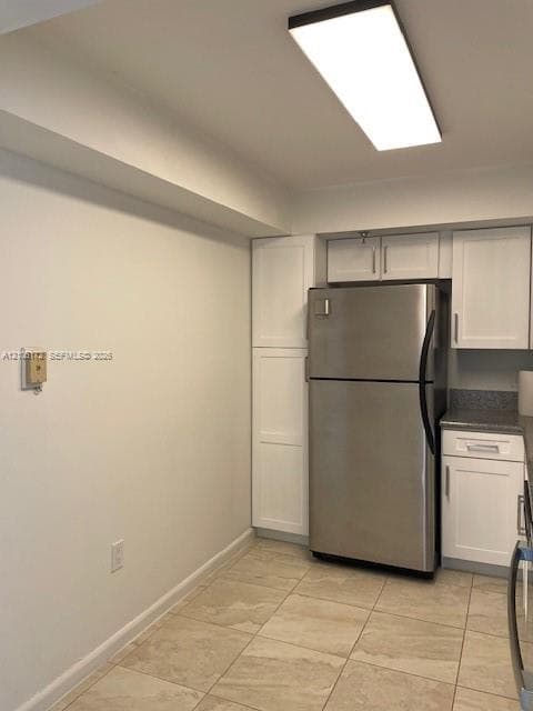 Kitchen featuring white shaker-style cabinetry, stainless steel refrigerator, stone-composite countertops, and large-format tile flooring