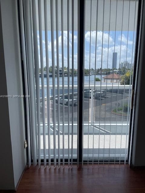 Sliding glass door with vertical blinds, wood-finish flooring, and exterior balcony featuring a metal railing