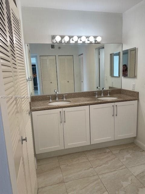Double vanity featuring white cabinetry, stone-finish countertops, dual drop-in sinks, polished metal hardware, and a full-width wall mirror