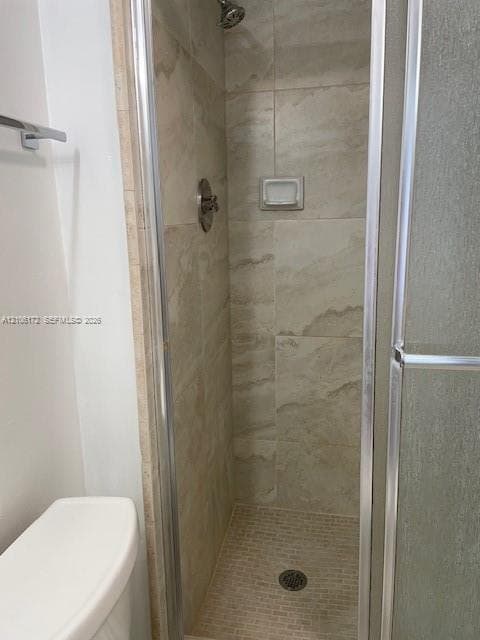Walk-in shower featuring floor-to-ceiling stone-finish wall tile, mosaic tile shower floor, integrated recessed soap dish, metal-frame glass door, and adjustable shower head