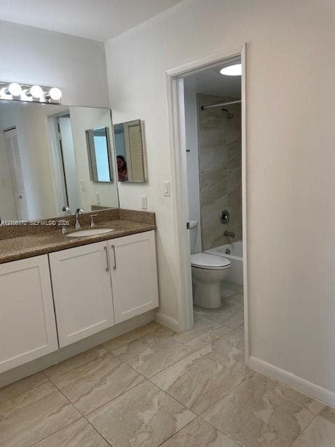 Bathroom featuring white shaker-style cabinetry, a stone-finish countertop with an integrated basin, large-format tile flooring, and a tub-shower combination with tiled surround