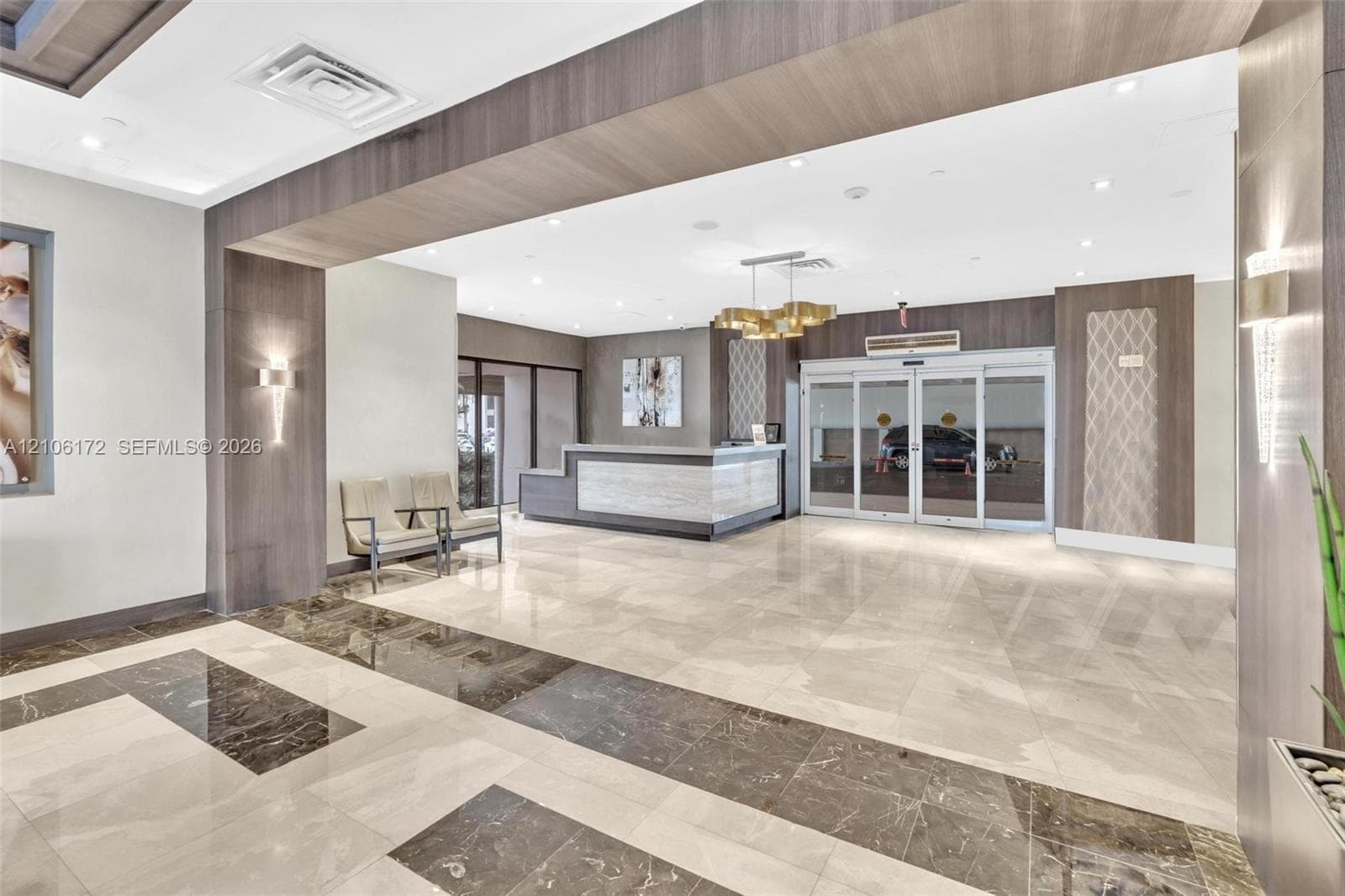 Entrance lobby featuring polished stone flooring, custom stone reception desk, recessed ceiling lighting, wood-finish wall paneling, and glass sliding entry doors