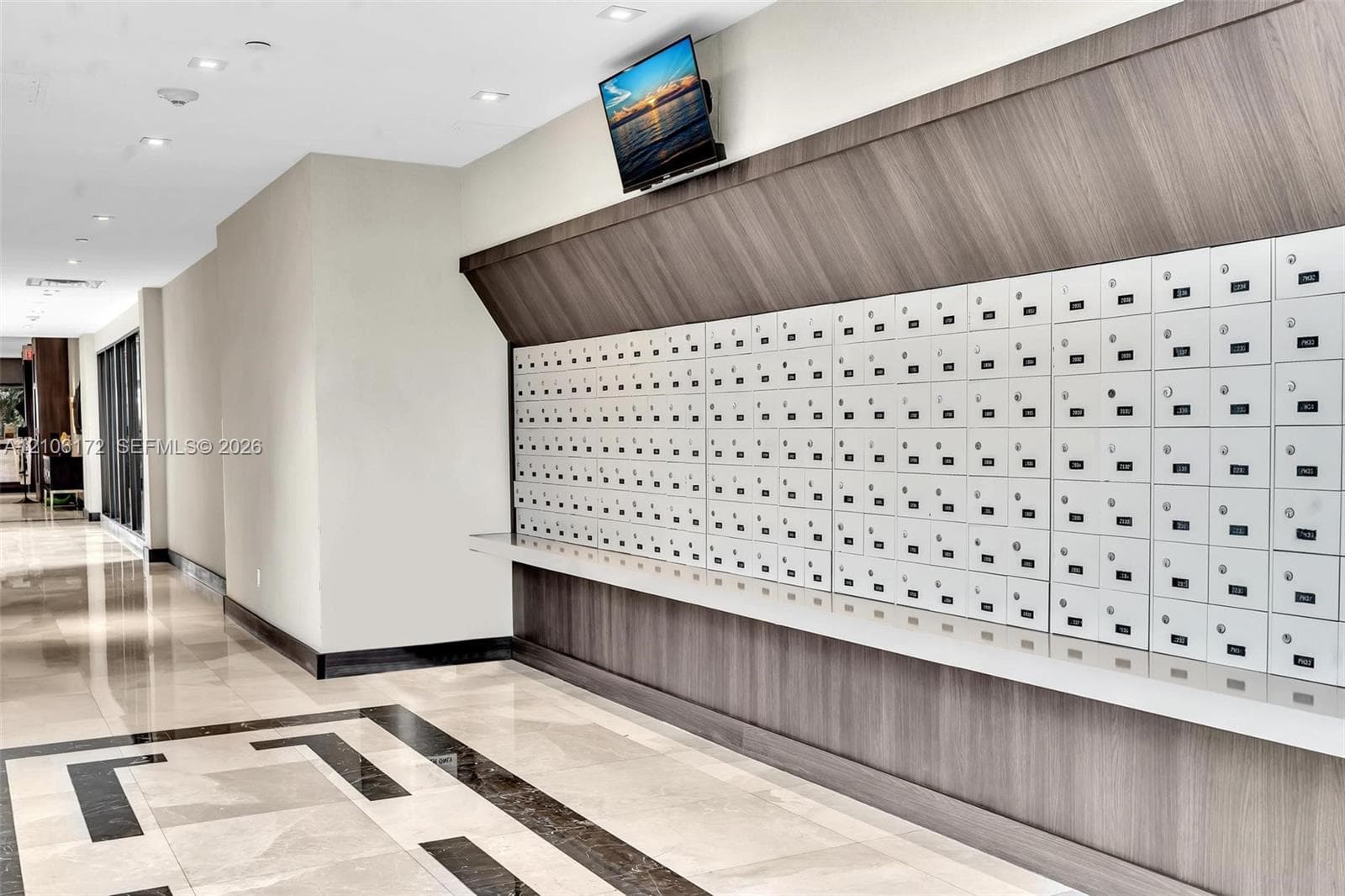 Mail center featuring high-capacity integrated parcel lockers, wood-finish paneling, polished stone flooring with geometric tile inlay, and recessed ceiling lighting