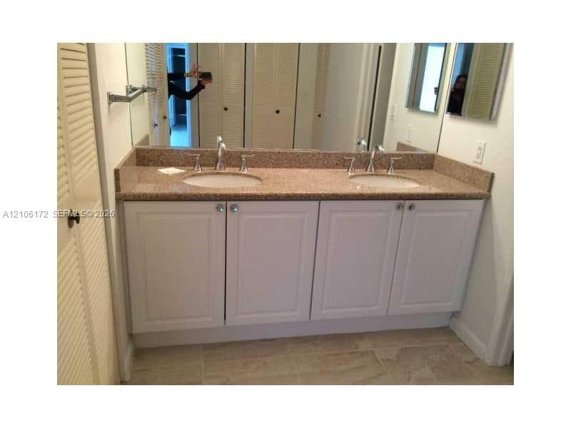 Dual vanity featuring a neutral-toned stone countertop, white cabinetry with silver-tone hardware, undermount sinks, and wall-to-wall mirror