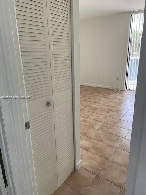 Bi-fold louvered closet doors, neutral ceramic tile flooring, and vertical blinds covering a floor-to-ceiling glass door