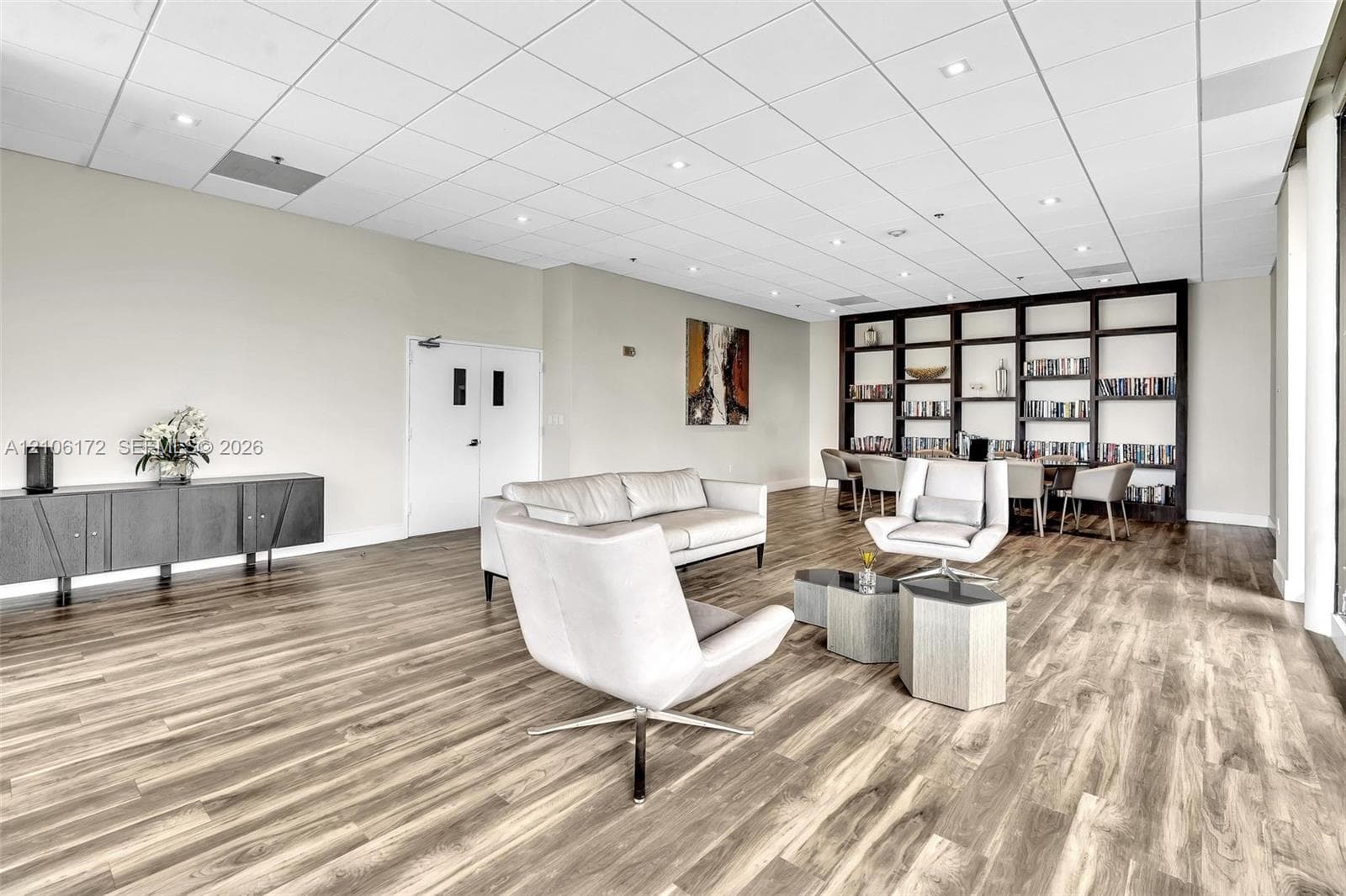 Expansive interior featuring wood-finish flooring, a full-height built-in dark wood shelving unit, recessed lighting, and a drop-tile ceiling