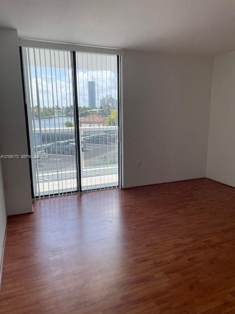 Wood-finish flooring and floor-to-ceiling sliding glass doors with vertical blinds, providing natural light and exterior water scenery