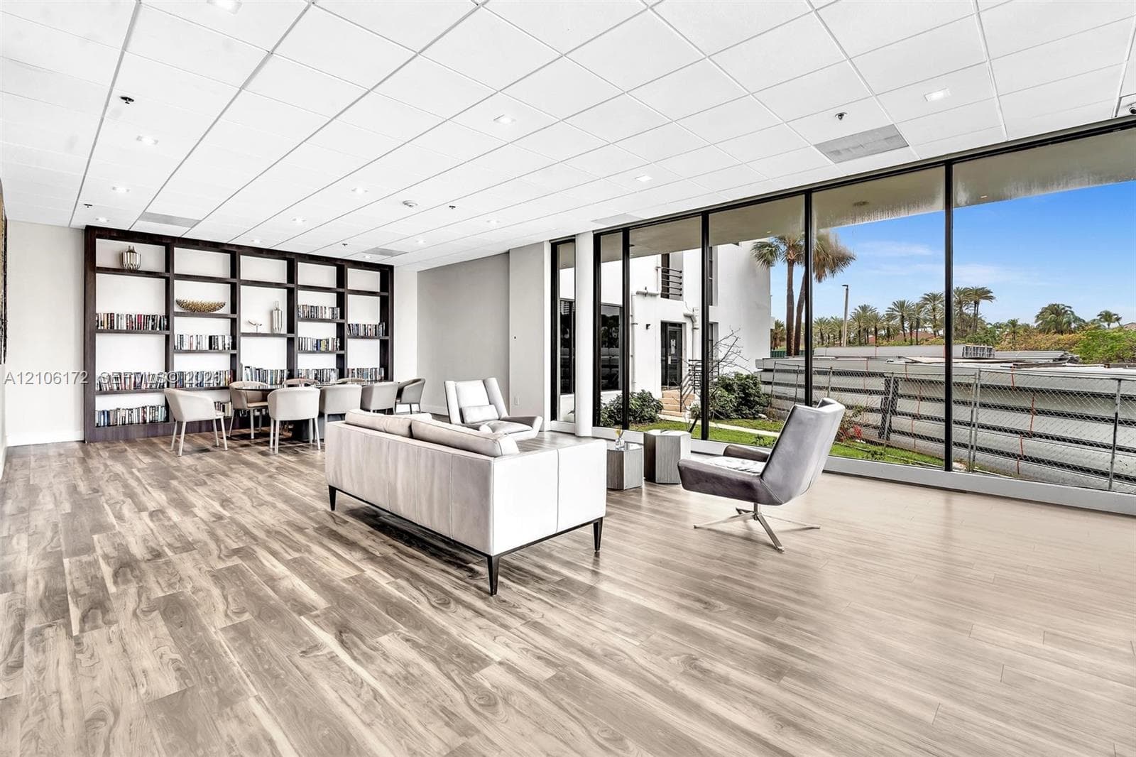 Open-concept interior featuring wood-finish flooring, floor-to-ceiling glass panel windows, recessed lighting, drop ceiling panels, and built-in wall shelving