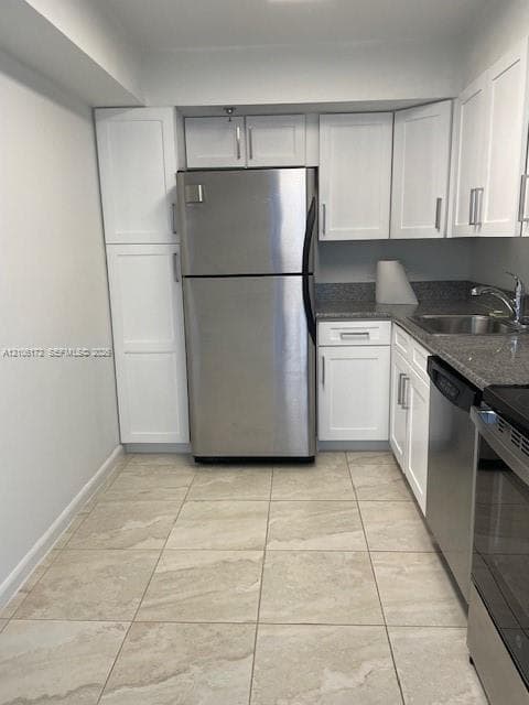 Kitchen featuring white shaker-style cabinetry, stainless steel appliances, neutral stone-finish tile flooring, and contrasting stone-finish countertops
