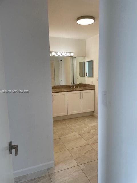 Bathroom featuring white shaker-style cabinetry, solid-surface countertop with dual integrated sinks, large vanity mirror, multi-bulb overhead lighting, and neutral floor tiling
