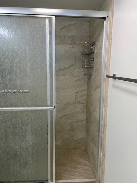 Shower enclosure featuring a sliding glass door, floor-to-ceiling neutral-toned tile surround, mosaic tile flooring, and integrated metal shelving