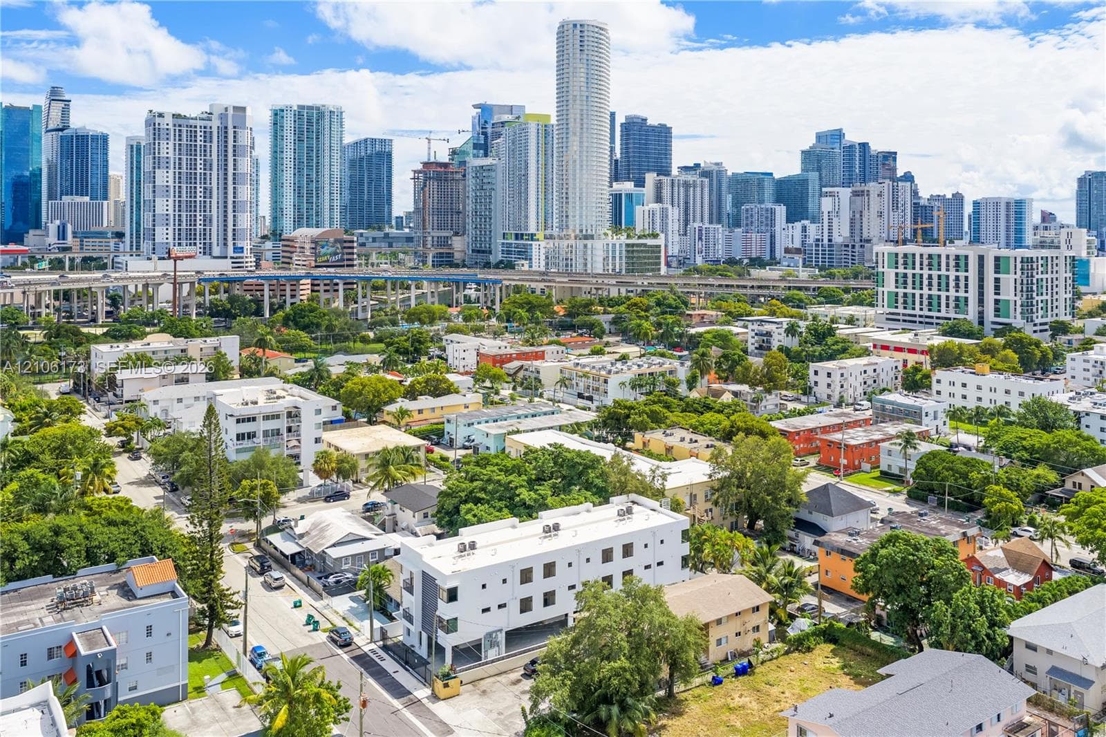 Aerial perspective featuring a multi-level white residential structure, mature landscaping, and an expansive cityscape backdrop