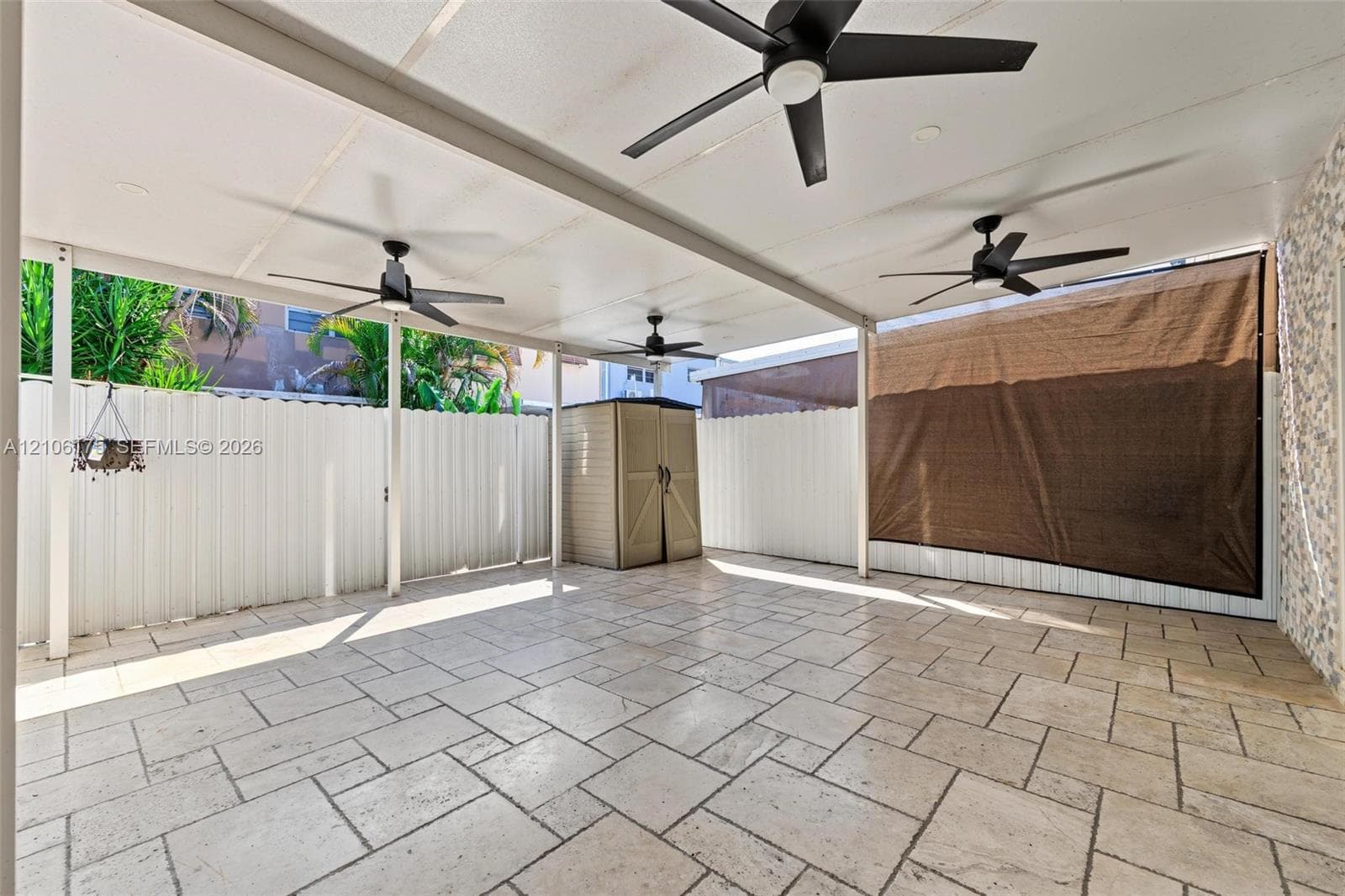 Covered patio featuring stone-tile flooring, three ceiling fans, and a white privacy fence