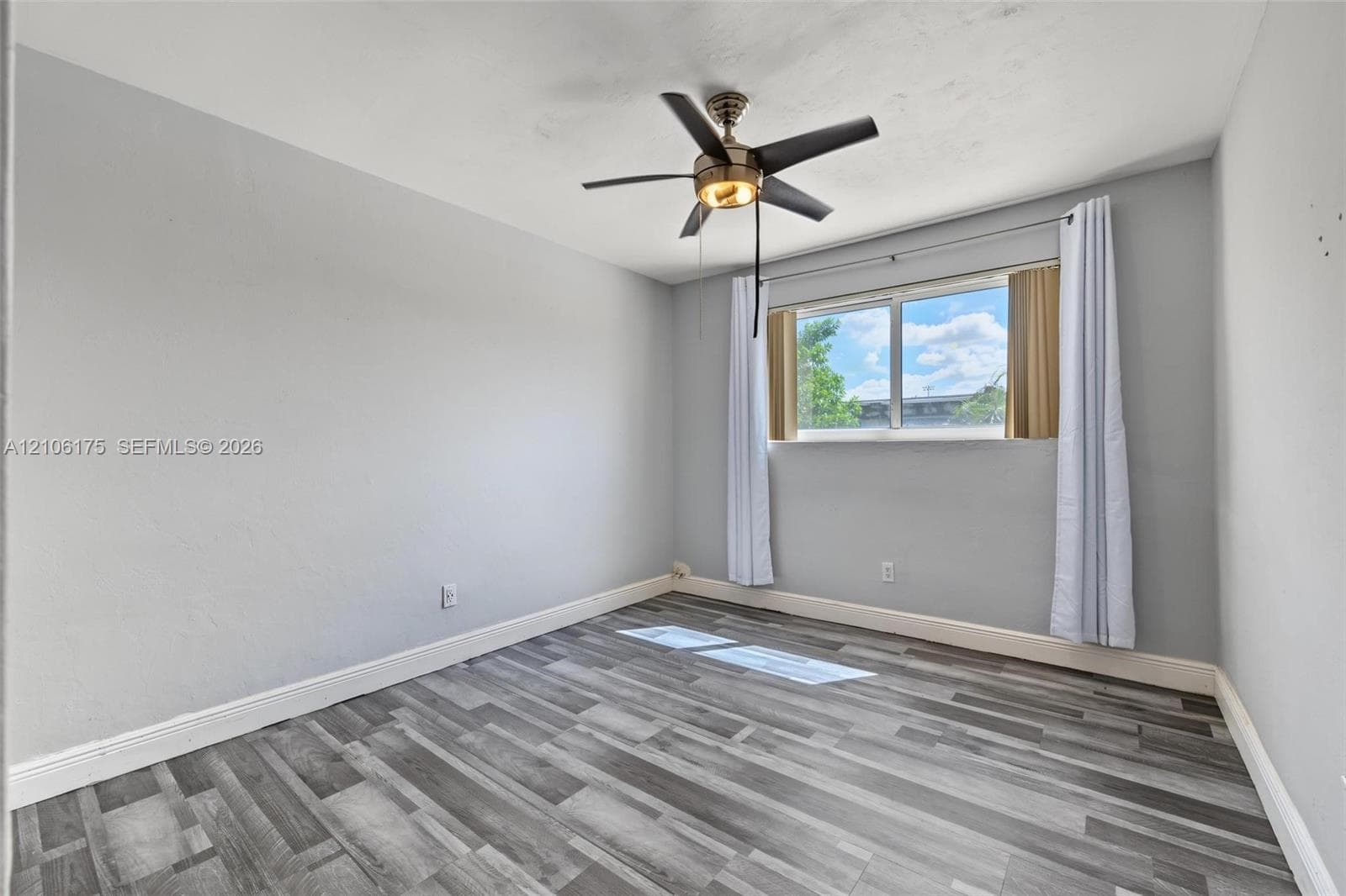 Neutral-toned interior featuring wood-finish flooring, a multi-blade ceiling fan with integrated lighting, and a single-pane window