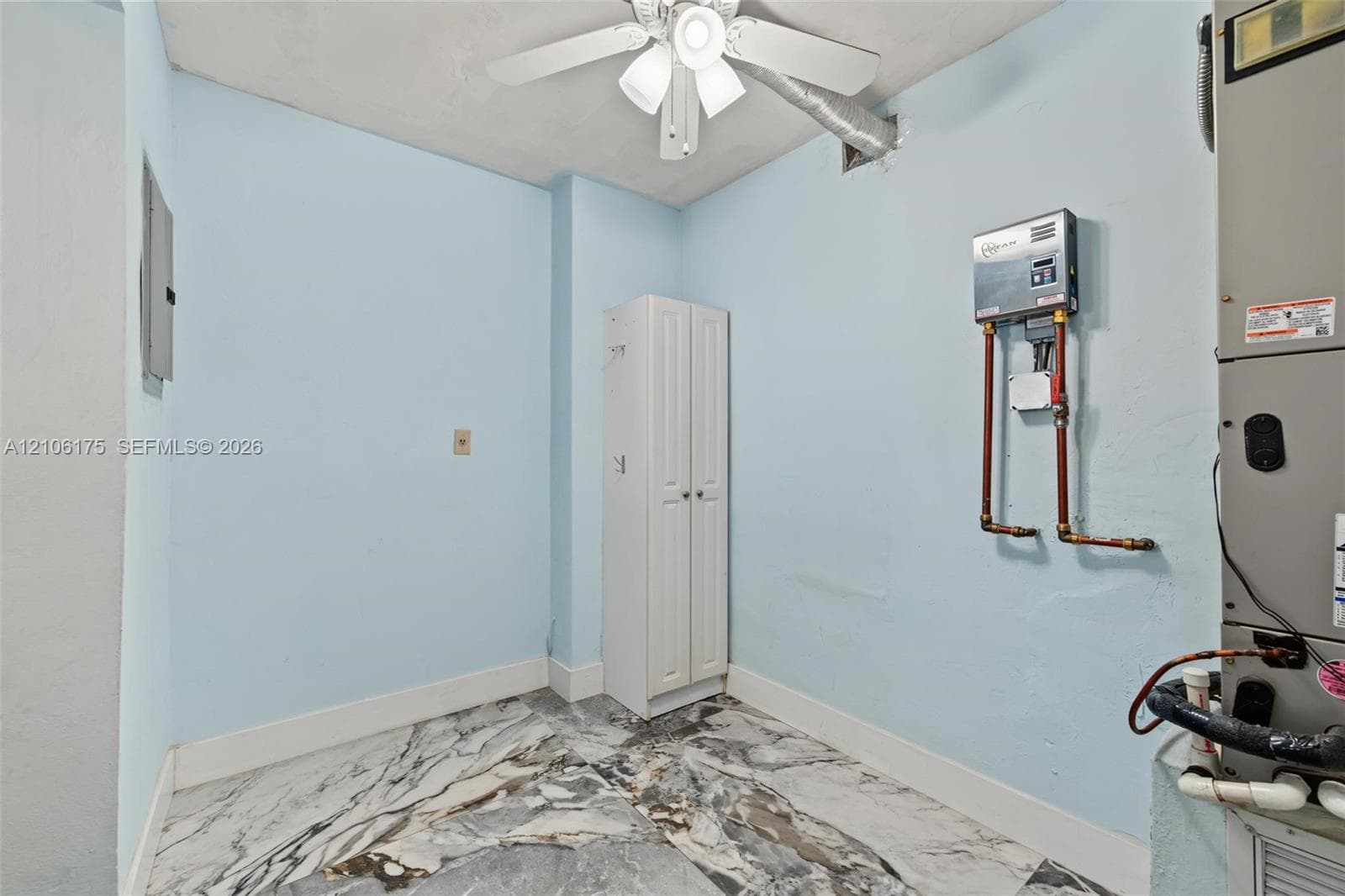 Utility area featuring large-format patterned stone-finish flooring, a ceiling-mounted fan with integrated light, a built-in vertical storage cabinet, and a wall-mounted water treatment system