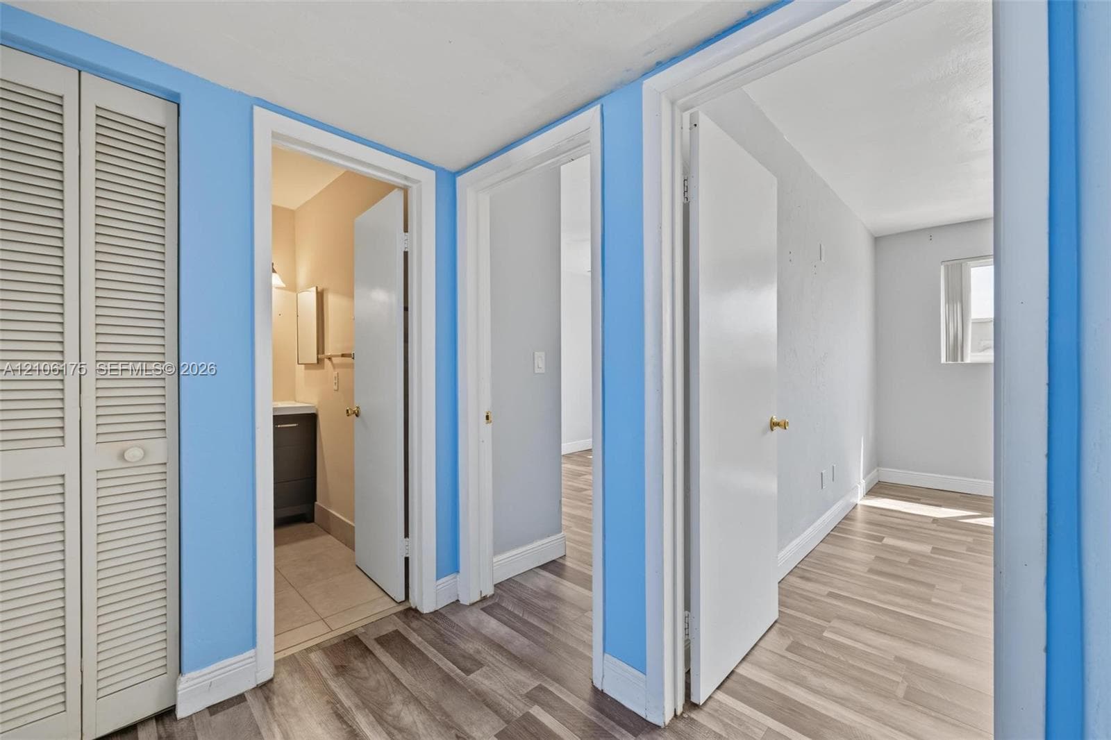 Interior hall featuring louvered bi-fold closet doors, wood-finish flooring, and multiple doorways leading to interior rooms