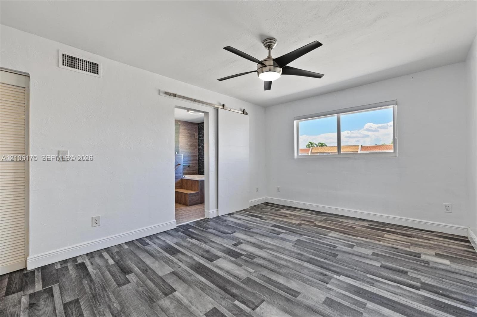 Room featuring wood-finish flooring, a sliding barn-style door, and a ceiling fan with integrated lighting