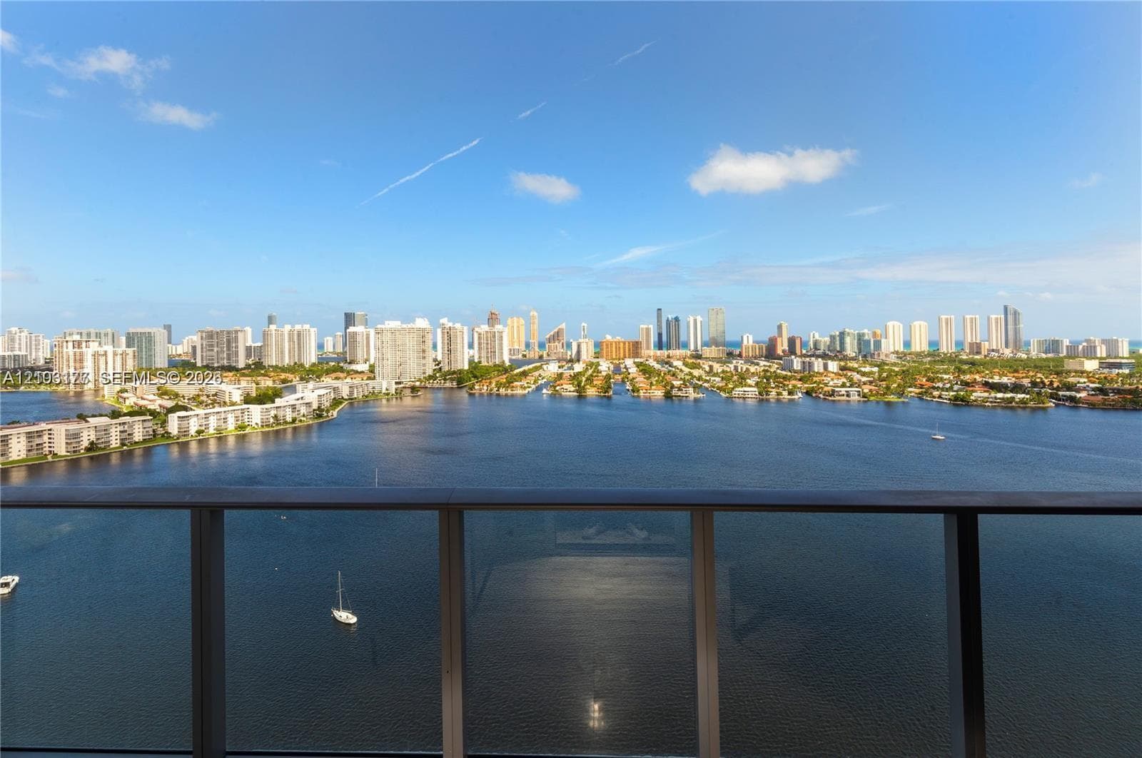 Glass balcony railing overlooking a bay, canal-front properties, and a city skyline