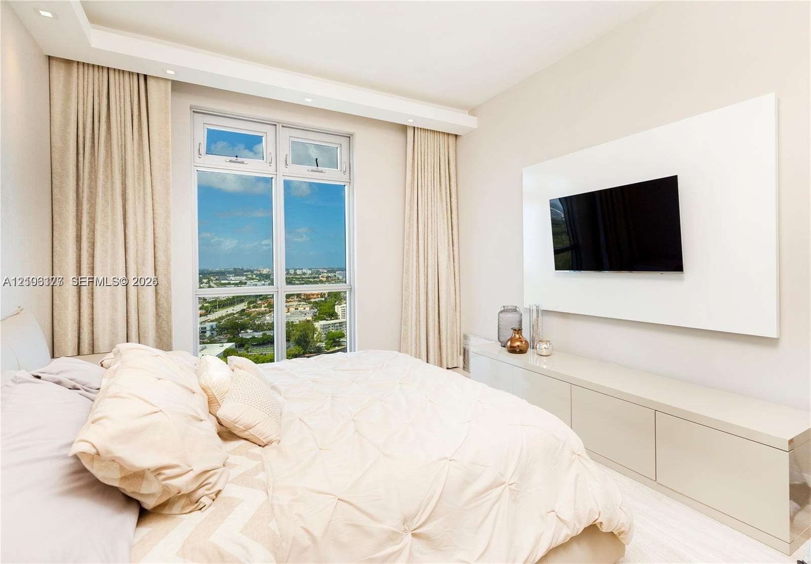 Floor-to-ceiling windows featuring panoramic exterior scenery, recessed ceiling lighting, and a custom built-in media console with a minimalist panel wall mount