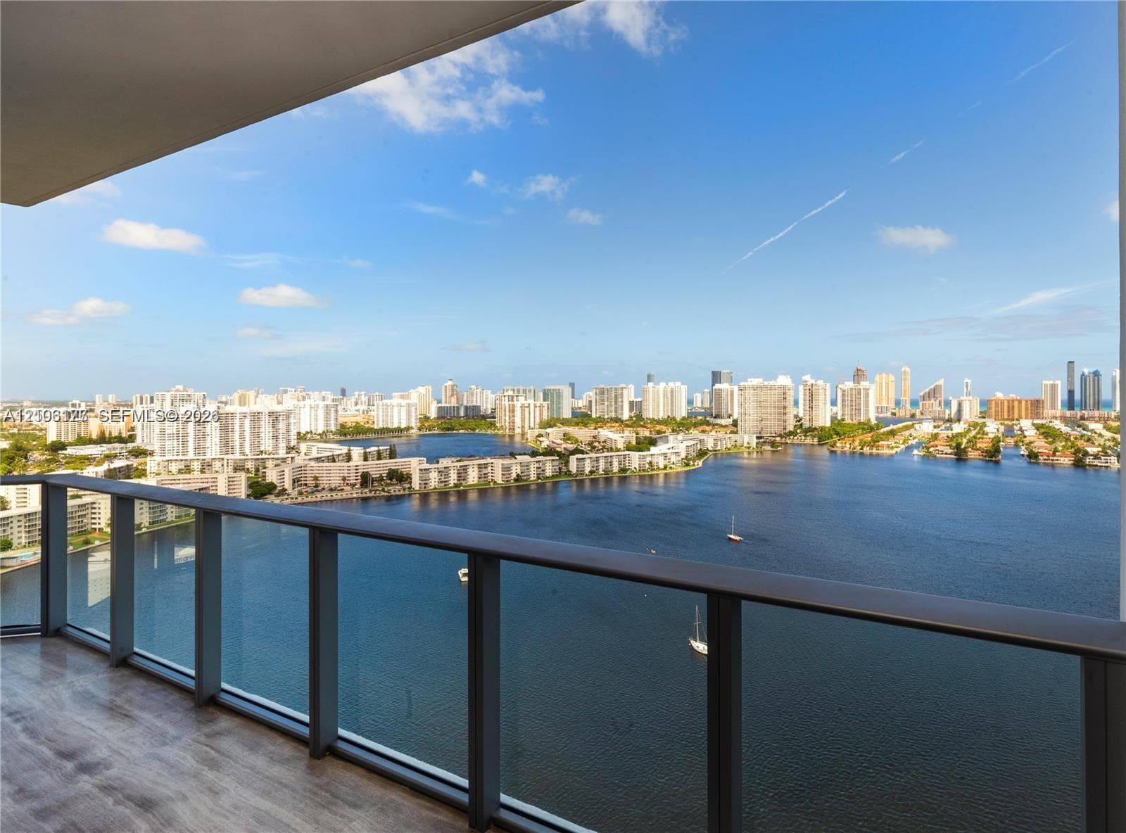 Covered balcony featuring wood-finish flooring and a glass railing with expansive water and city skyline horizon