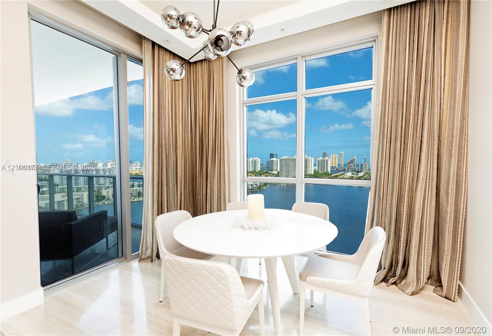 Floor-to-ceiling windows, polished light-toned flooring, tray ceiling with recessed lighting, and a multi-globe contemporary chandelier