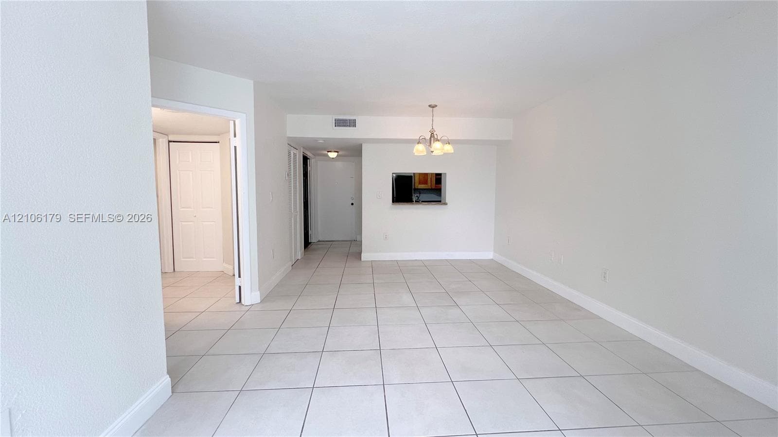 Neutral-toned ceramic tile flooring, multi-arm chandelier lighting, and kitchen pass-through window with interior ledge
