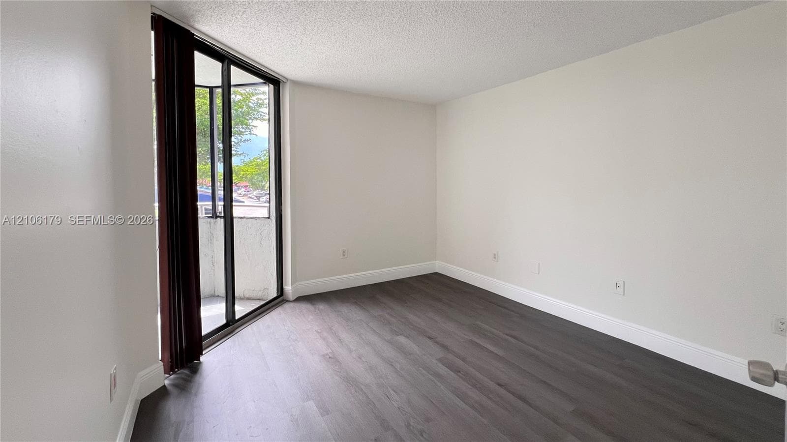 Room featuring wood-finish flooring, neutral wall paint, and full-height glass sliding doors accessing a private balcony