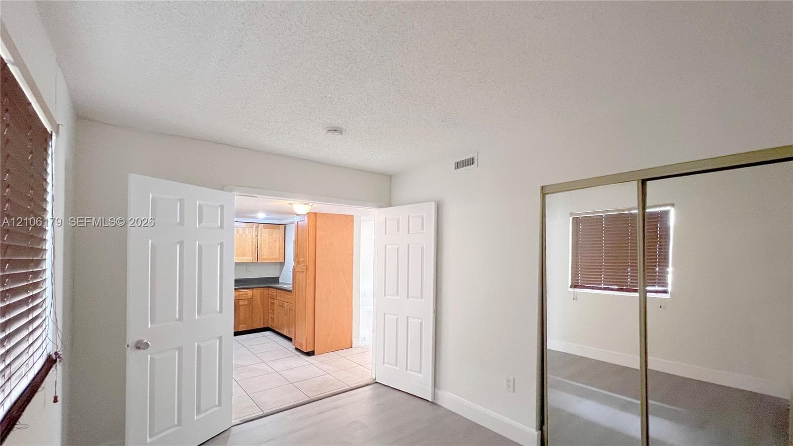 Interior space featuring light-toned flooring, wood-finish kitchen cabinetry, tile flooring in the kitchen, double-door entry, and sliding mirror-panel closet doors