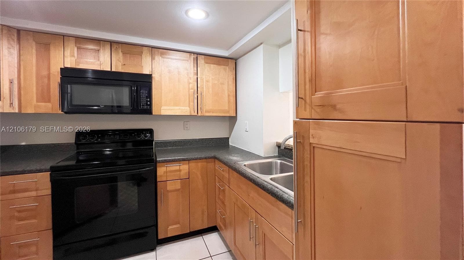 Kitchen featuring light wood-finish cabinetry, dark solid-surface countertops, black integrated microwave, black oven range, and stainless steel double-basin sink