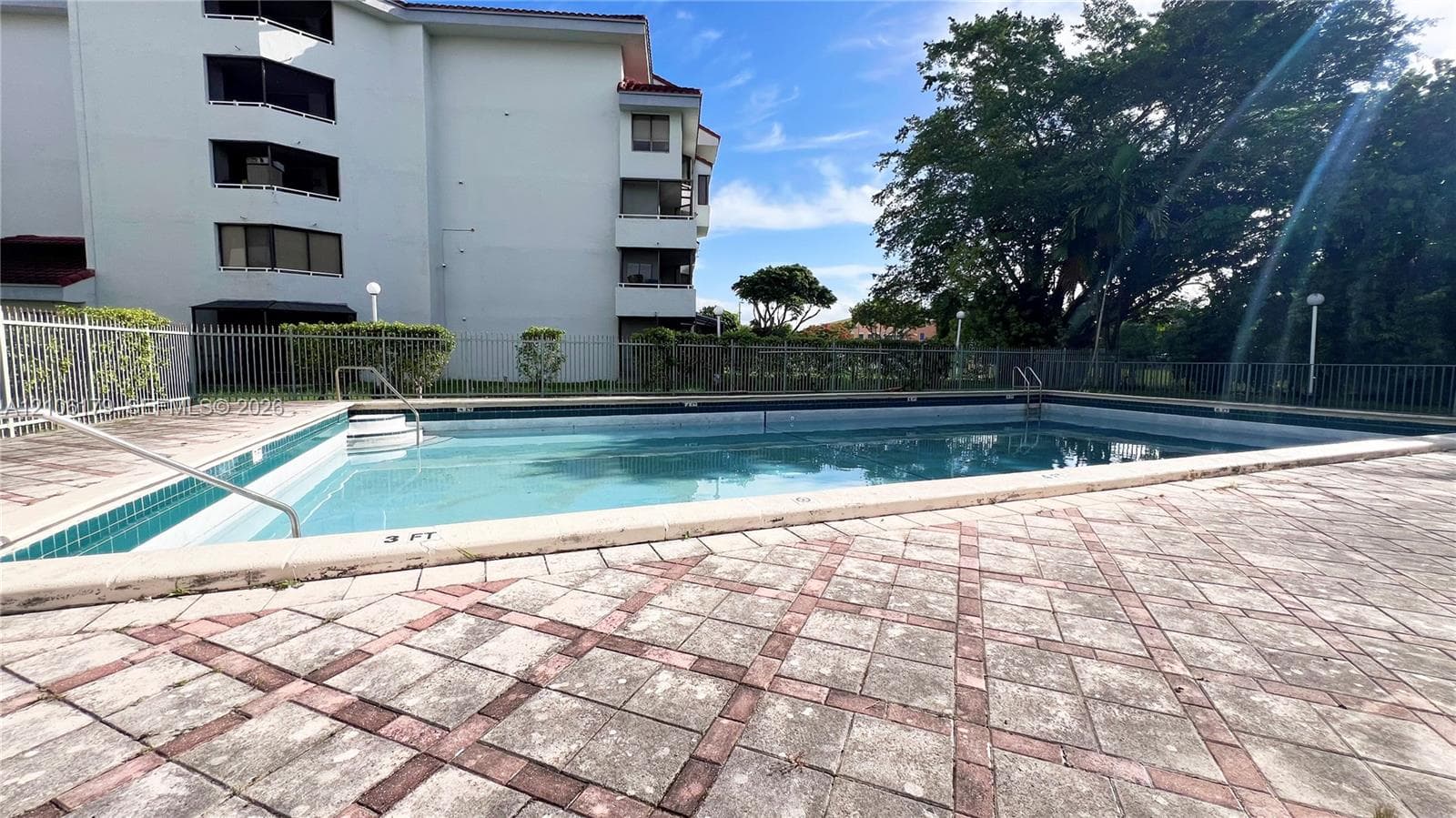 Outdoor swimming pool featuring a concrete deck with a patterned tile border and a metal safety fence enclosure