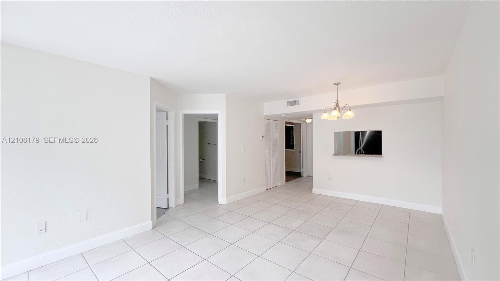 Neutral-toned interior featuring large-format tile flooring, a multi-bulb chandelier, a built-in wall niche, and crisp, light-colored walls