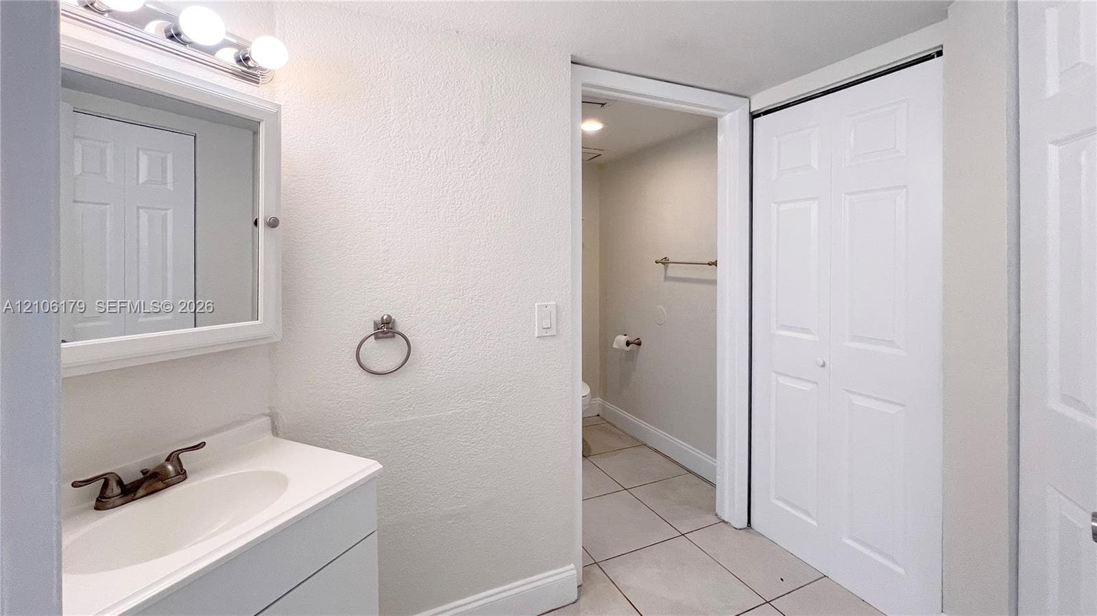Bathroom featuring a vanity with an integrated basin, metal finish faucet, tri-bulb vanity light, mirrored medicine cabinet, and tile flooring