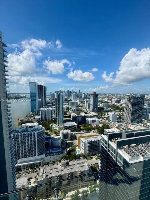 High-rise balcony with a structural glass railing overlooking an expansive urban skyline, coastal waterway, and surrounding metropolitan area