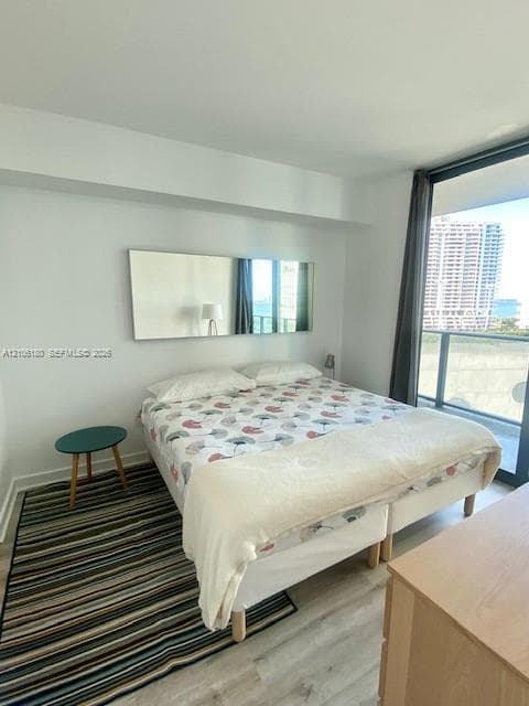 Floor-to-ceiling windows, private balcony access, neutral wall finishes, and wood-finish flooring