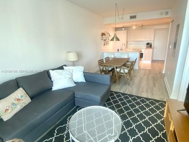 Open-concept living space featuring wood-finish flooring, white cabinetry, a peninsula countertop, and metallic pendant lighting