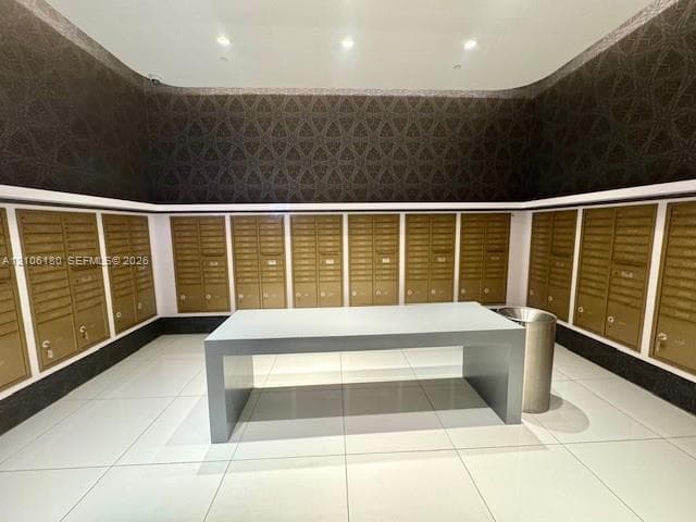 Mailroom featuring floor-to-ceiling geometric wallpaper, large-format tile flooring, recessed ceiling lighting, a central freestanding console, and metallic finish mailboxes