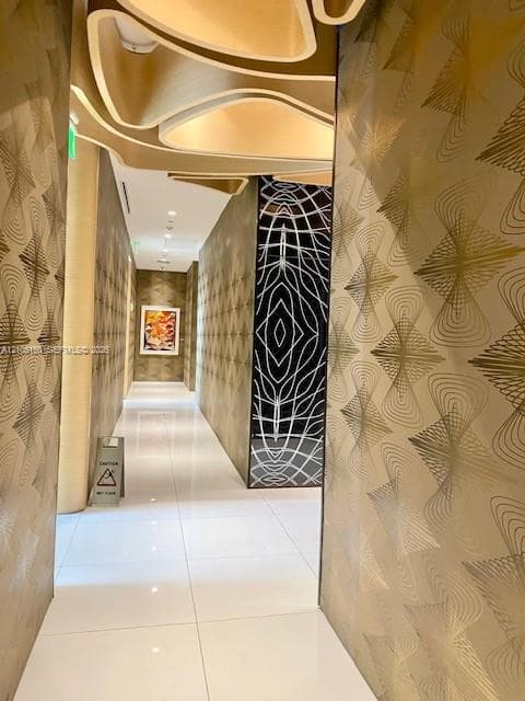 Hallway featuring large-format tile flooring, textured geometric wall coverings, and a sculptural, tiered ceiling element