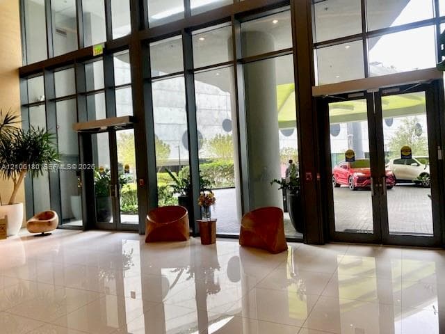 Double-height lobby featuring floor-to-ceiling glass panel walls, dual glass-paned entry doors, polished tile flooring, and metal framing