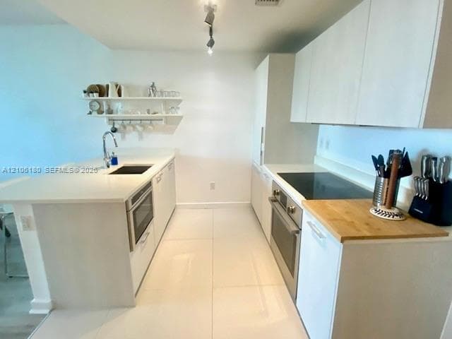 Modern kitchen featuring flat-panel cabinetry, light-toned stone countertops, a stainless steel under-mount sink, integrated appliances, and overhead track lighting