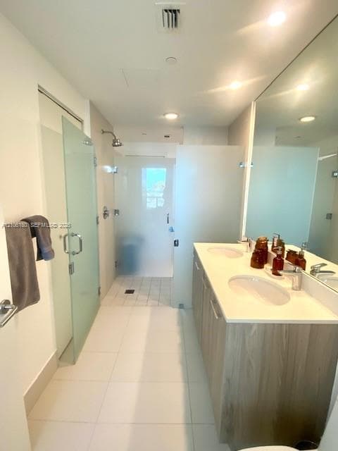 Dual-sink vanity with light wood-finish cabinetry, solid-surface countertop, full-width wall mirror, and walk-in shower with frosted glass enclosure