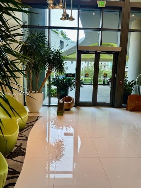 Lobby entrance featuring floor-to-ceiling glass paneling, polished tile flooring, and metallic pendant lighting